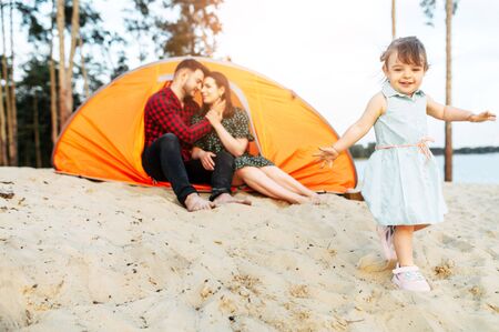 Family time outdoors in a forest. Young parents and cute toddler girl spend active time together, they are living in a camp in a forestの写真素材