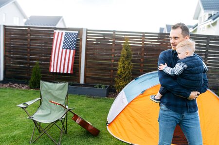 Father is carrying his toddler in the arms outdoors. Games in the backyardの写真素材