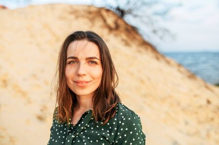 A young attractive woman in a green polka dress outdoors. A beautiful woman is walking on wild seashoreの写真素材