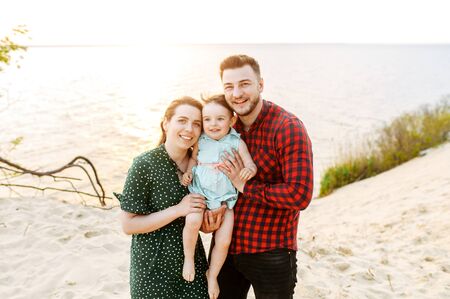Happy together. Young parents and cute baby girl outdoors. Mom and dad are holding their daughter in handsの写真素材