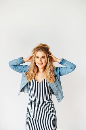 Gorgeous beauty. Beautiful young blonde woman in striped dress smiles and looks at camera, she holds head with her handsの写真素材