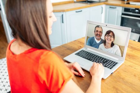 Video meeting with a parents. A senior couple on the laptop screen, a young woman talking online with them. Back viewの写真素材