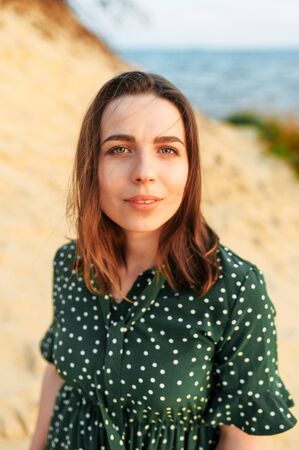 Close-up portrait of young beautiful girl outdoors. A brunette girl in green polka dress is looking at the cameraの写真素材