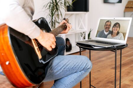 A guy plays guitar at home and demonstrates this to parents via video connect, a senior couple on the laptop screen. Online performance, video callの写真素材