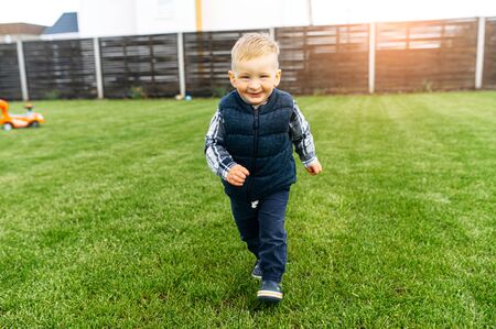 Laughing toddler boy is running on the green lawn outdoors. Happy childhoodの写真素材