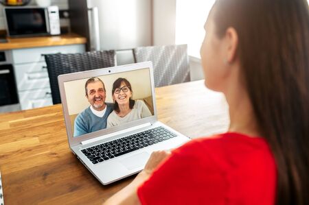 Video meeting with a parents. A senior couple on the laptop screen, a young woman talking online with them. Back viewの写真素材