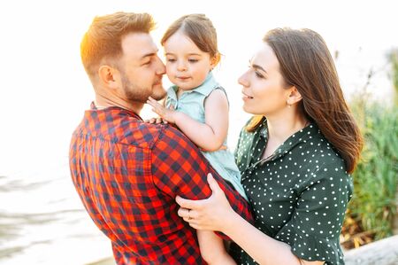 Portrait of happy young family. A young mother and father hold their cute daughter on their arms outdoorsの写真素材