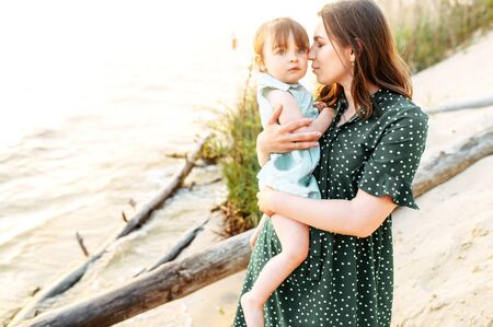 Mothers love. A young beautiful mother tenderly holds cute daughter on her arms outdoorsの写真素材