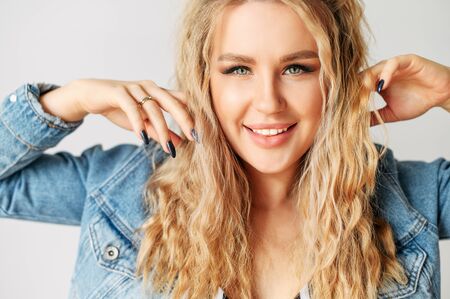 Playful beautiful woman in a jeans jacket on a white background, she runs her fingers trough her hair.の写真素材