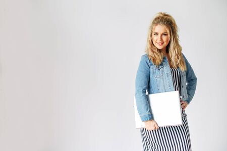 Isolated on a white background picture of attractive girl in casual wear with a laptop, she smiles and looks at cameraの写真素材