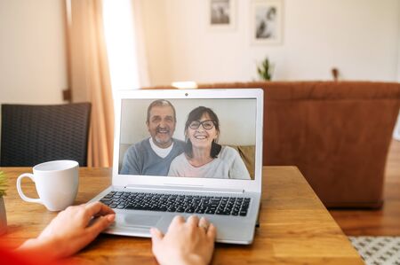 Video call with a parents. A senior couple on the laptop screen, female hands on the keyboardの写真素材
