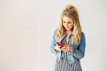 Isolated on white background picture of young attractive woman chatting on phone. A girl in casual jeans jacket is typing messages on a phone screenの写真素材