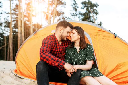 A young married couple hug in a tent outdoors. Couple in love spend time in a forest campの写真素材