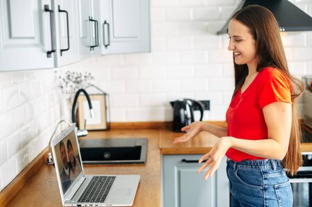 A young woman with a laptop in the kitchen at home, she talks online with a family. Video call with parentsの写真素材