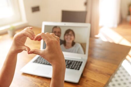 Video chat with a parents. Female hands are showing heart shape to parents on the laptop screen. Video call, love signの写真素材