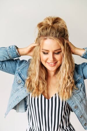 Vertical orientation portrait of attractive well-groomed young woman on a white background, she is touching her blonde hair hands. Fashion posing, model in studioの写真素材