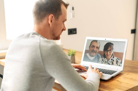 Virtual meeting with a parents. A young man is using laptop for video call to senior couple.の写真素材