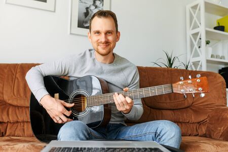 Webcam shot of handsome guy playing acoustic guitar. Video call, online performanceの写真素材