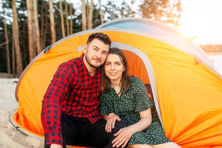 Couple in love spend time in a camp in the forest, they are sitting and hugging in an orange tent. Tourists, campersの写真素材
