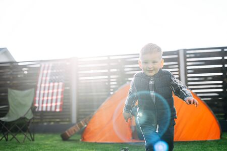 Smiling baby boy with blonde hair walks on a green lawn in warm sunlightの写真素材