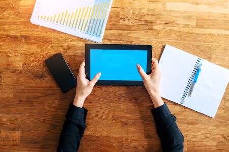Top view of female hands hold a digital tablet on a wooden table. A screen of tablet is blank, copy space for text.の写真素材