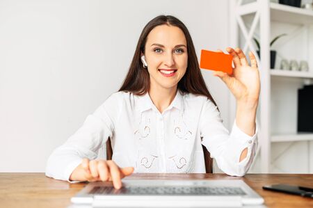 Online shopping. Webcam shot of young cheerful woman, she is showing a credit card and smiles at cameraの写真素材