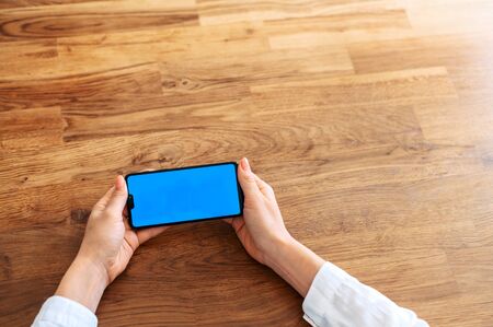 Close-up female hands is holding smartphone. A phone with a blue blank screen for inserting text in horizontal position. Copy spaceの写真素材