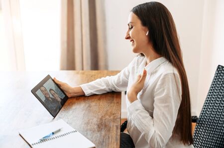 Video appointment online with family psychologist, doctor. A woman in formal white shirt is communicating via video with a couple on the tablet screen. Video meetingの写真素材
