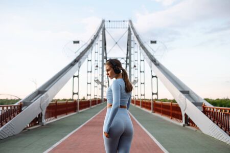 Sport with a favorite soundtracks. Side view young woman in sportswear with a headphones on the bridge in sunset light. Running outdoorの写真素材