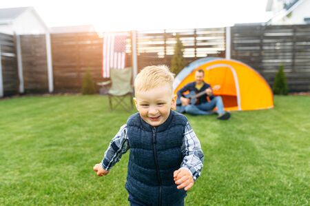 Father and toddler son spend time together in the backyard. A boy is running and laughing, father...