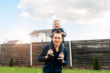 Father and son are happy to spend time together outdoors. Dad is carrying his little son on the shoulders, they laughの写真素材