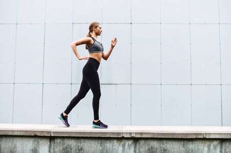 Cheerfulness for full day long. An attractive young woman is jogging outdoors. Side view. Healthy lifestyle conceptの写真素材