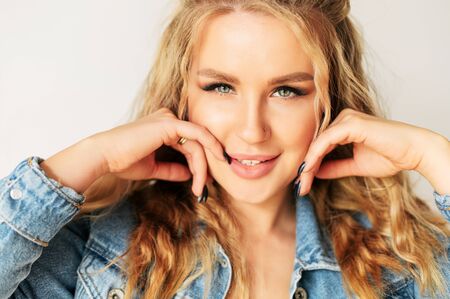Close-up portrait of well-groomed attractive blonde woman with a curly hair, she is holds hands with a trendy manicure near face. Beauty industry conceptの写真素材