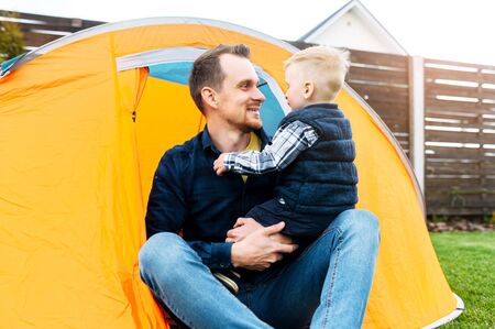Father and son play camp in the backyard. Young father and his little toddler boy are playing together in an orange tent outdoorsの写真素材