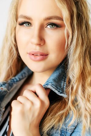 Close-up portrait of young attractive blonde woman with a curly hair, she has fresh face skin and trendy make-up. Vertical pictureの写真素材