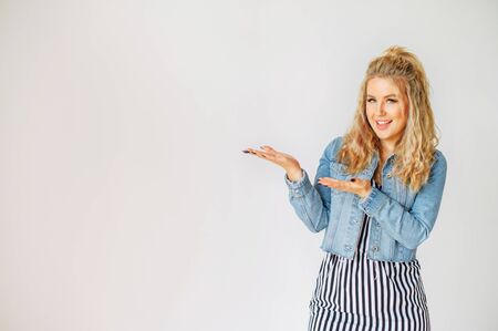 Just look at here. Beautiful blonde girl in casual wear points hands to empty space for text. Studio shot on white backgroundの写真素材