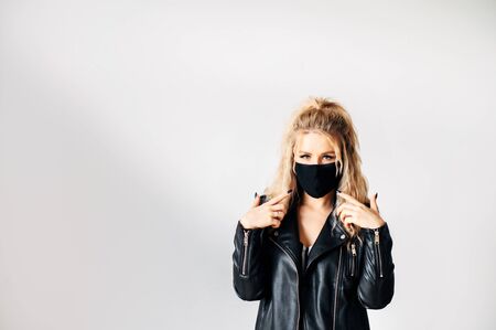 Protection against viral threats. Woman in black clothes with a surgical mask on her face shows fingers on a maskの写真素材