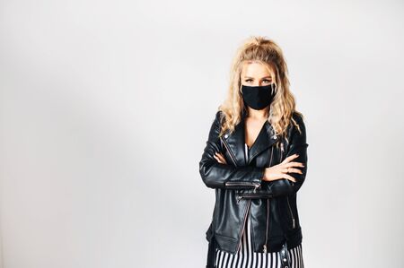 Protect yourself during an epidemic. Young blond woman in a leather jacket in a medical mask on her face on a white backgroundの写真素材