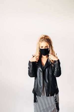 Protection against viral threats. Woman in black clothes with a surgical mask on her face shows fingers on a maskの写真素材