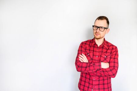 Handsome guy in red plaid shirt with eyeglasses stands with arms crossed on white background. Copy space for your textの写真素材