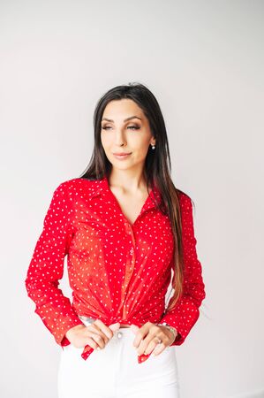 Pretty young brunette woman in red shirt looks away, isolated on white background. Vertical shotの写真素材