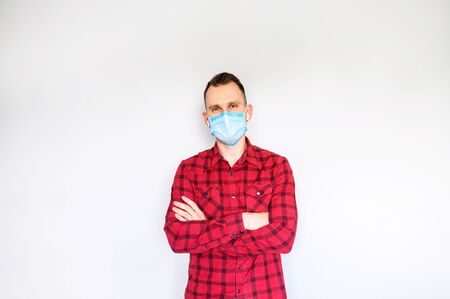 Confident guy in casual wear with surgery mask on the face stands with arms crossed, isolated on gray backgroundの写真素材
