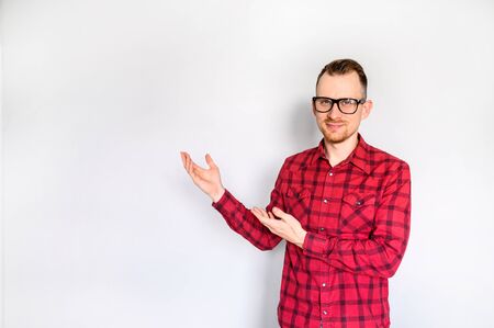 Handsome guy in red plaid shirt with eyeglasses points hands on empty copyspaceの写真素材