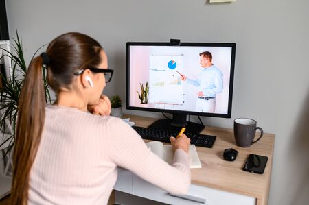 Webinars, lectures online. A woman in office is watching online classes, male teacher on laptop screen. Professional development, business trainingの写真素材