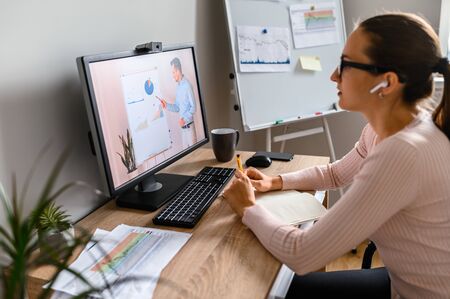 Webinars, lectures online. A woman in office is watching online classes, male teacher on laptop screen. Professional development, business trainingの写真素材