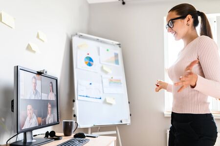 Webinar, online meeting, presentation. A young woman speaks to the online audience via video call, video connection. She stands in front of pc screen with online viewers, flip chart on the backgroundの写真素材