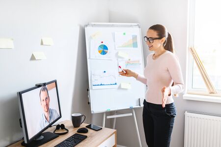Video meeting of employees. A young woman in glasses talks to young man on pc screen, she widely spreads her arms, distant work.の写真素材
