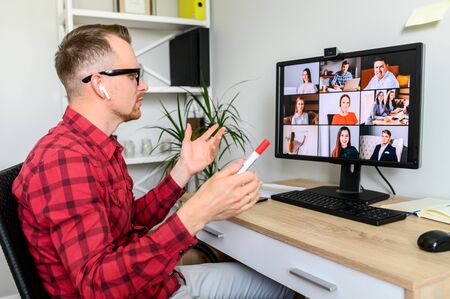 Online meeting, conference call. Young confident man is using PC software for video communication with employees. Man in glasses sits at the desk and talks online, he holds a marker in his handの写真素材