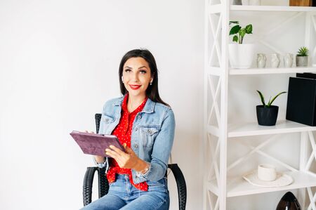 Attractive young woman sitting on a chair with a tablet in her hand. Home leisure in network, social mediaの写真素材