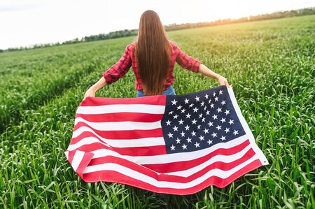 Waving in the wind an American flag in the hands of a young girl running on a green captive field, the back view. Independence dayの写真素材
